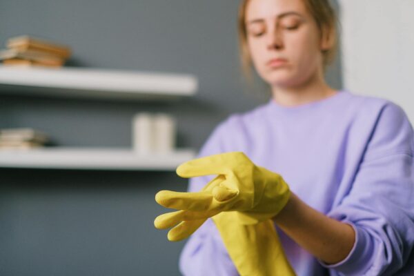 Crop blurred female in casual clothes putting on yellow latex gloves in light room in daytime